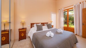 A bedroom with a bed, two bedside tables, a window with curtains, and a view of greenery outside. - Beautiful Finca with Wi-Fi, Pool, Lawn, and Patio; Parking Available (Son Servera)
