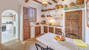 A kitchen with wooden beams, a white table with a plate of food, and shelves with pottery. - Holiday Home "Son Galiana" with Wi-Fi, Garden and Terrace (Montuïri)