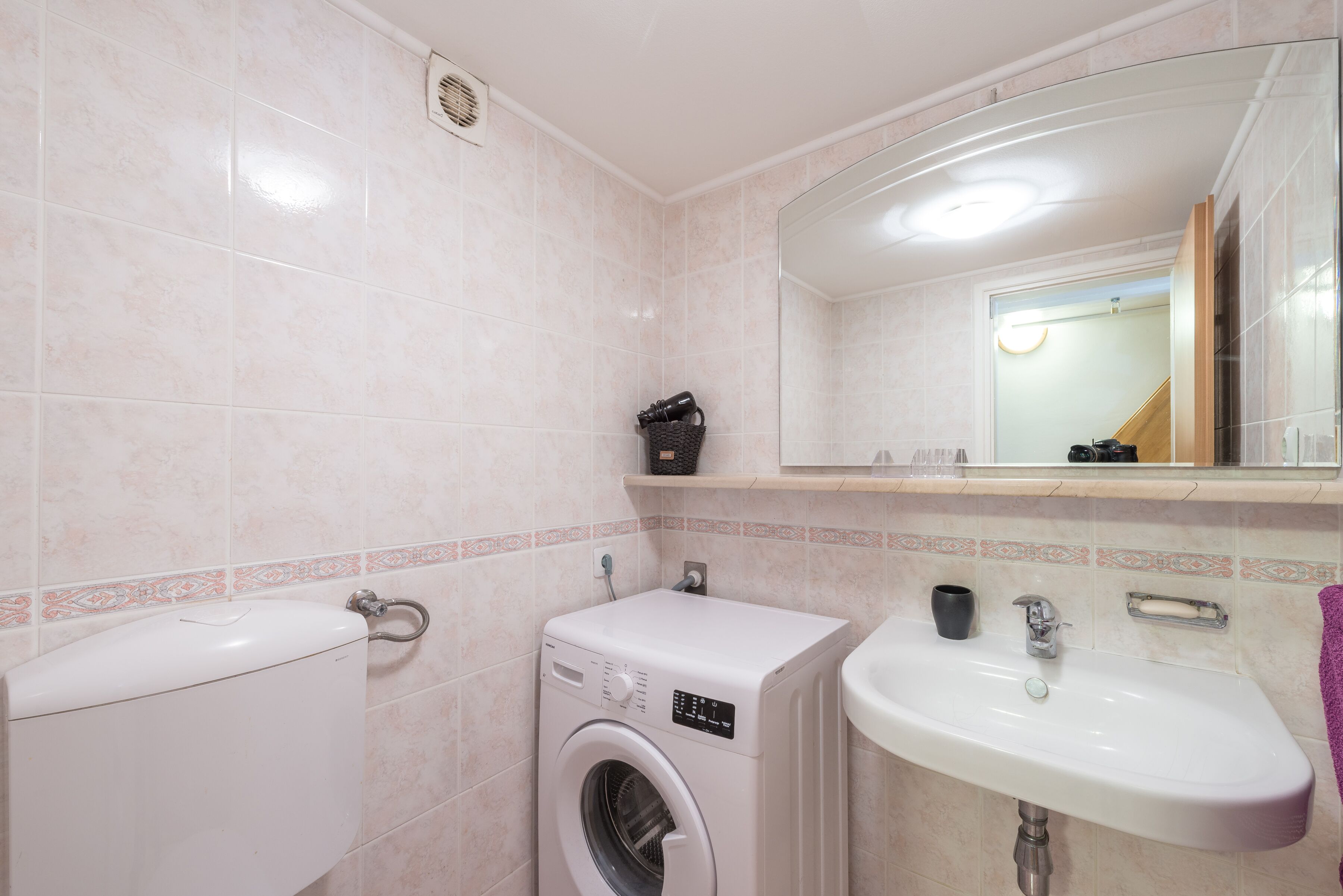 Un baño con inodoro, lavadora, lavabo y un espejo sobre el lavabo.
