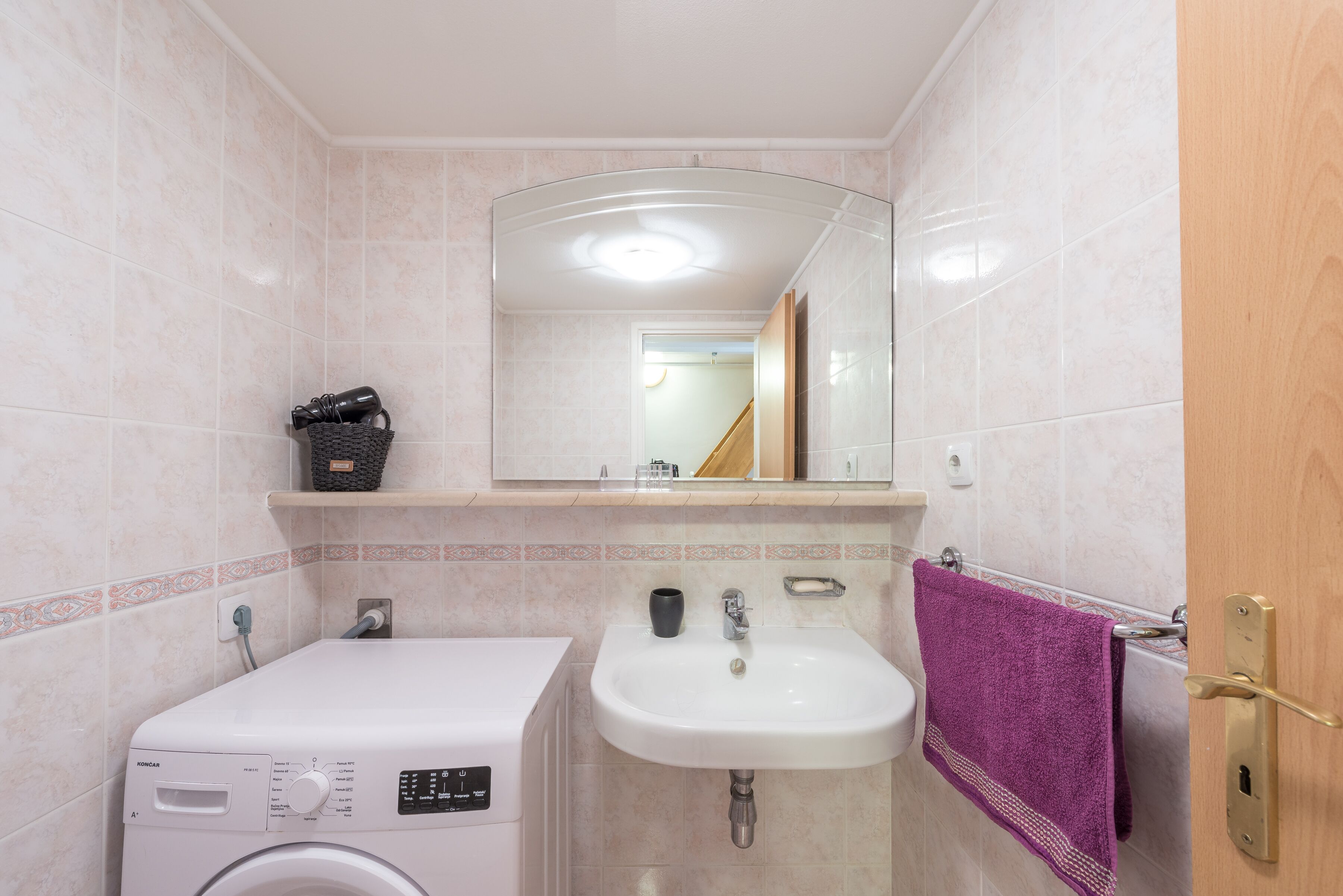 A compact bathroom with a washing machine, a sink, and a mirror.