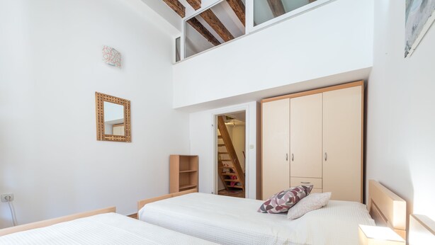 A bedroom with two beds, a wooden headboard, a mirror, and a wardrobe. - Apartment Old Writer (Dubrovnik)