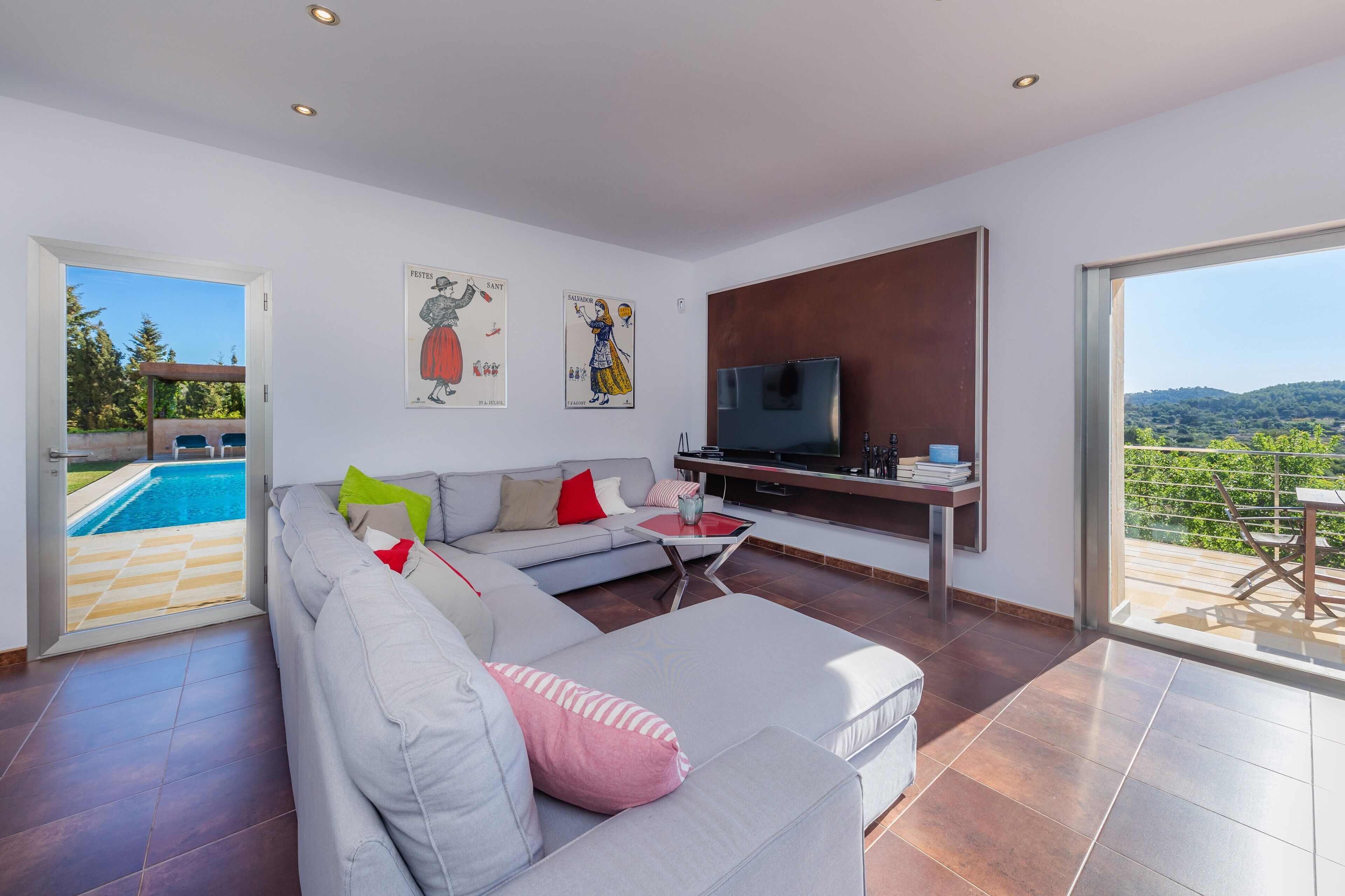 A modern living room with a large sofa, a TV, and a pool view.