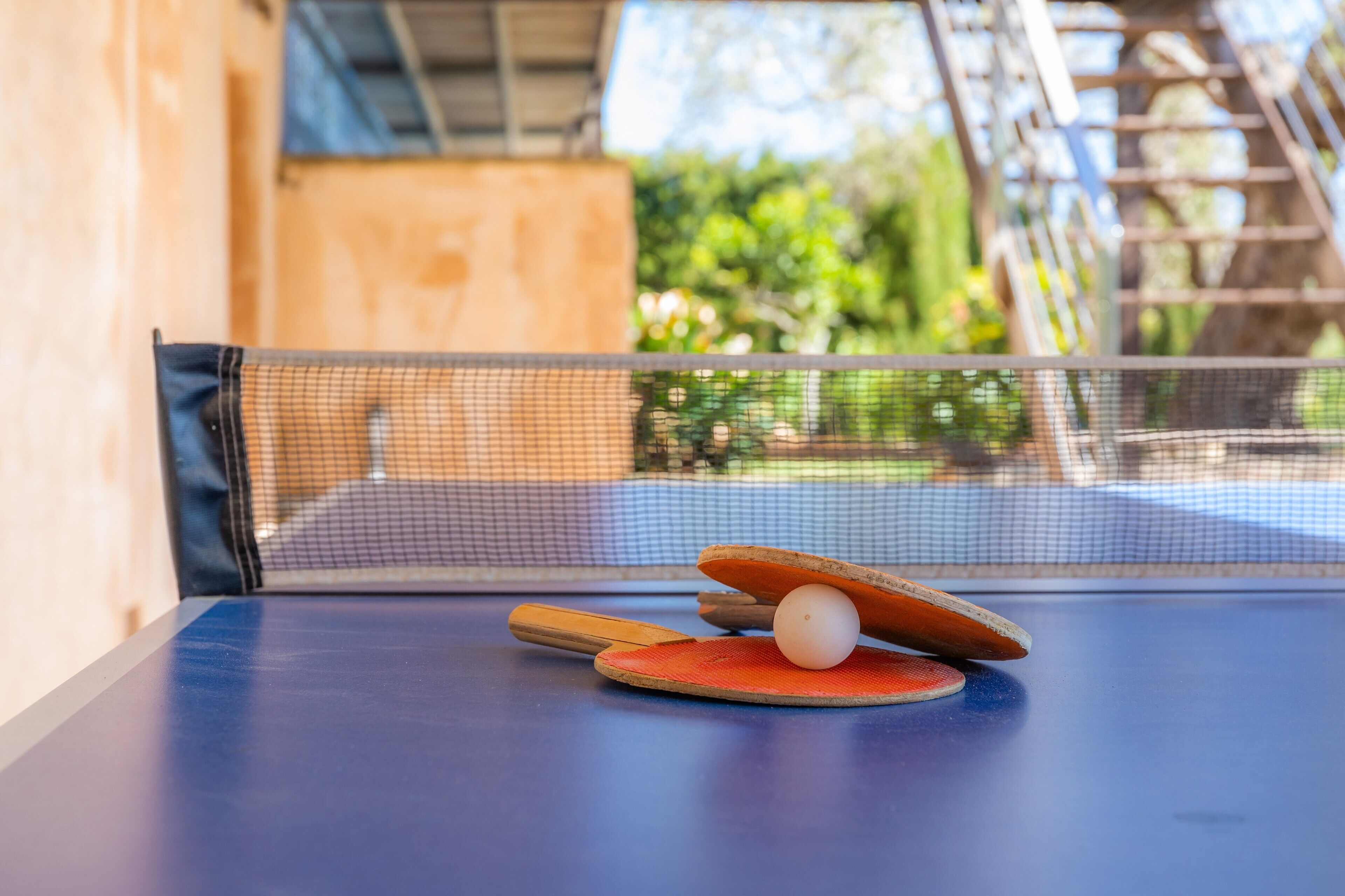 A table tennis setup with a net, paddle, and ball on a blue table.