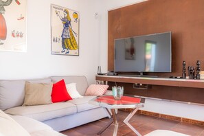 A modern living room with a sofa, a glass coffee table, a flat-screen TV, and artwork on the wall.