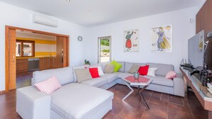 Un salon moderne avec un canapé d’angle, une table basse et un coin cuisine visible à travers une porte ouverte.