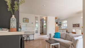 Una sala de estar con sofá, mesa de centro, piano y cocina al fondo.