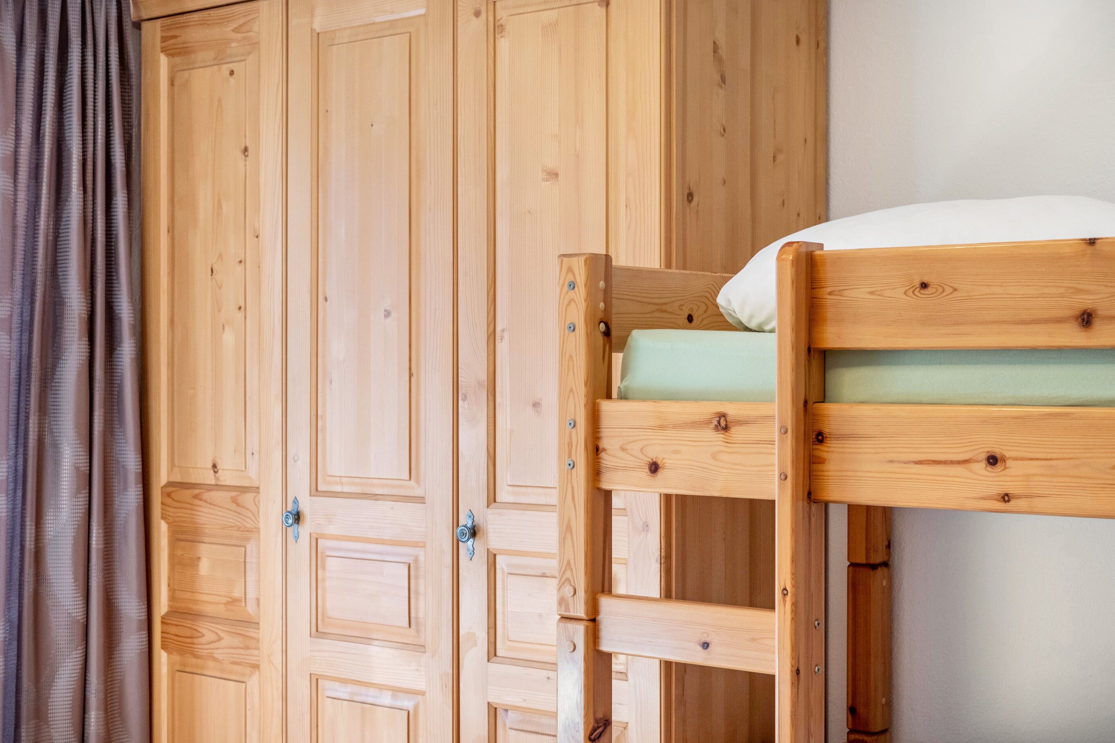 A bunk bed with a green mattress, wooden wardrobe, and a curtain.