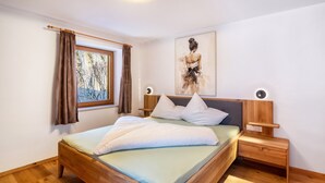 Un dormitorio con cama de madera, mesita de noche, lámpara de pared y ventana con cortinas.