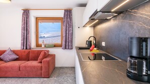 Un espacio habitable compacto con kitchenette, un sofá, una ventana con cortinas y vistas a un paisaje nevado.