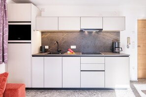 A modern kitchen with white cabinets, a black countertop, a built-in stove, and a coffee maker.