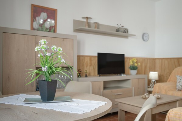 A modern living room with a round wooden table, a potted plant, a flat-screen TV, and a sofa.