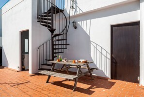 A patio with a wooden table and benches, a spiral staircase, and a door.