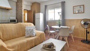 A living room with a sofa, a coffee table with decorative items, a dining area with a table and chairs, a kitchen area with a microwave, and a fan. - Family Friendly Apartment "Rocio" with Terrace, Air Conditioning and Wi-Fi (Conil de la frontera)