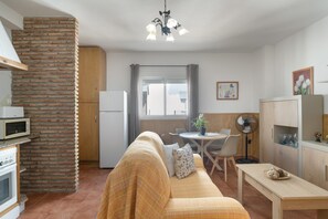 A compact kitchen with a microwave, a brick wall, a wooden cabinet, and a dining area with a table and chairs.