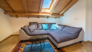 Une pièce de style loft avec un plafond en bois, un grand canapé d’angle, une table en verre et un tapis coloré.