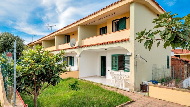 Un edificio residencial de dos plantas con techo de tejas, un balcón y un pequeño jardín.