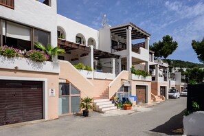 Une rue résidentielle bordée de bâtiments blancs, de balcons et de plantes en pot.