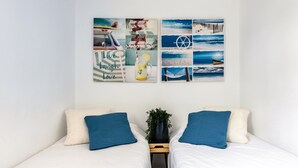 A bedroom with two beds, a wall with travel-themed artwork, and a small plant on the nightstand. - Holiday Home "Casita en Cala Llonga" with Sea View, Shared Garden & Pool (Cala Llonga)