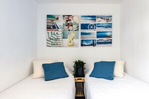 A bedroom with two beds, a wall with travel-themed artwork, and a small plant on the nightstand. - Holiday Home "Casita en Cala Llonga" with Sea View, Shared Garden & Pool (Cala Llonga)