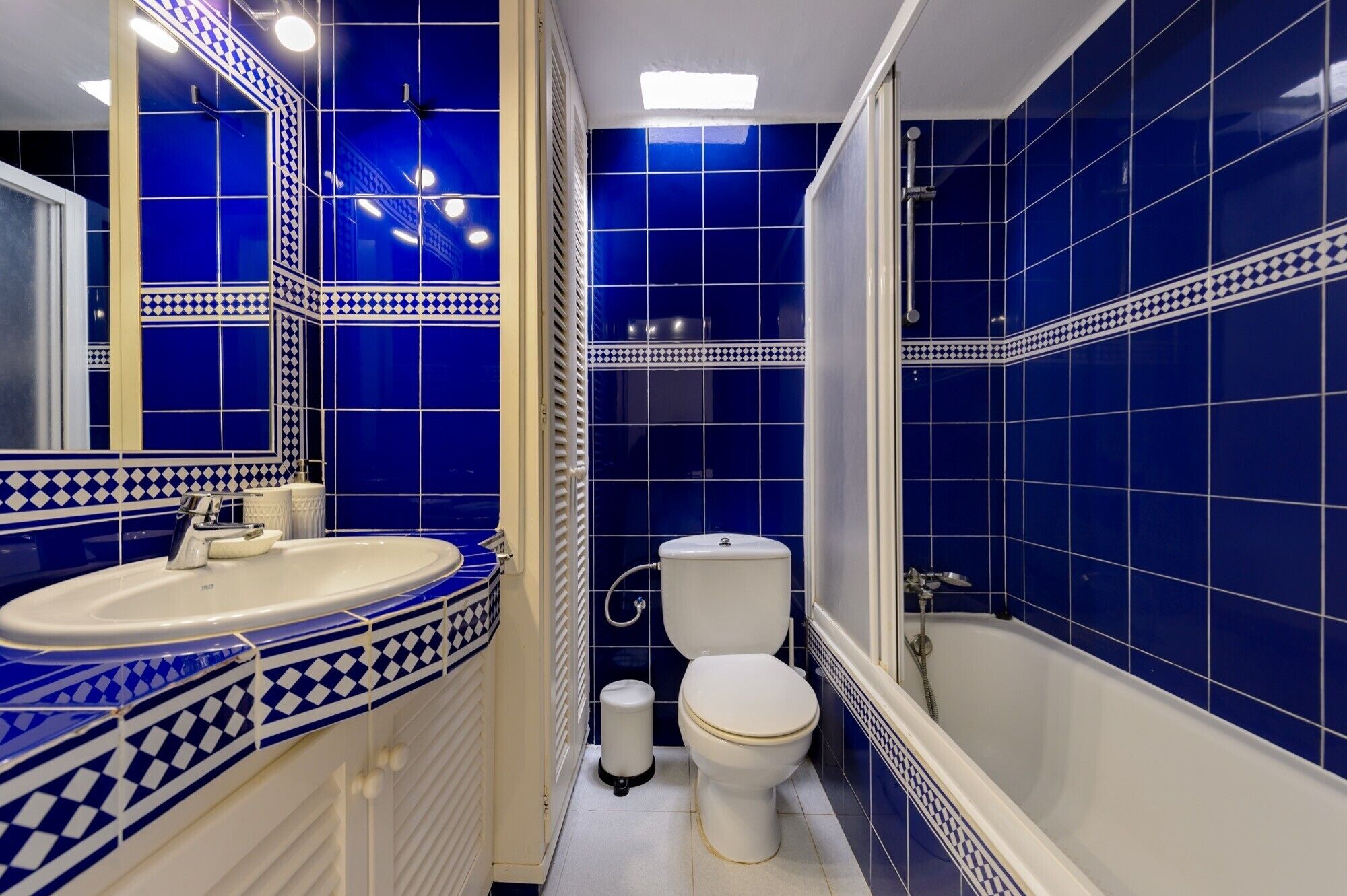 Un baño con paredes de azulejos azules, un lavamanos blanco, un inodoro y una bañera.
