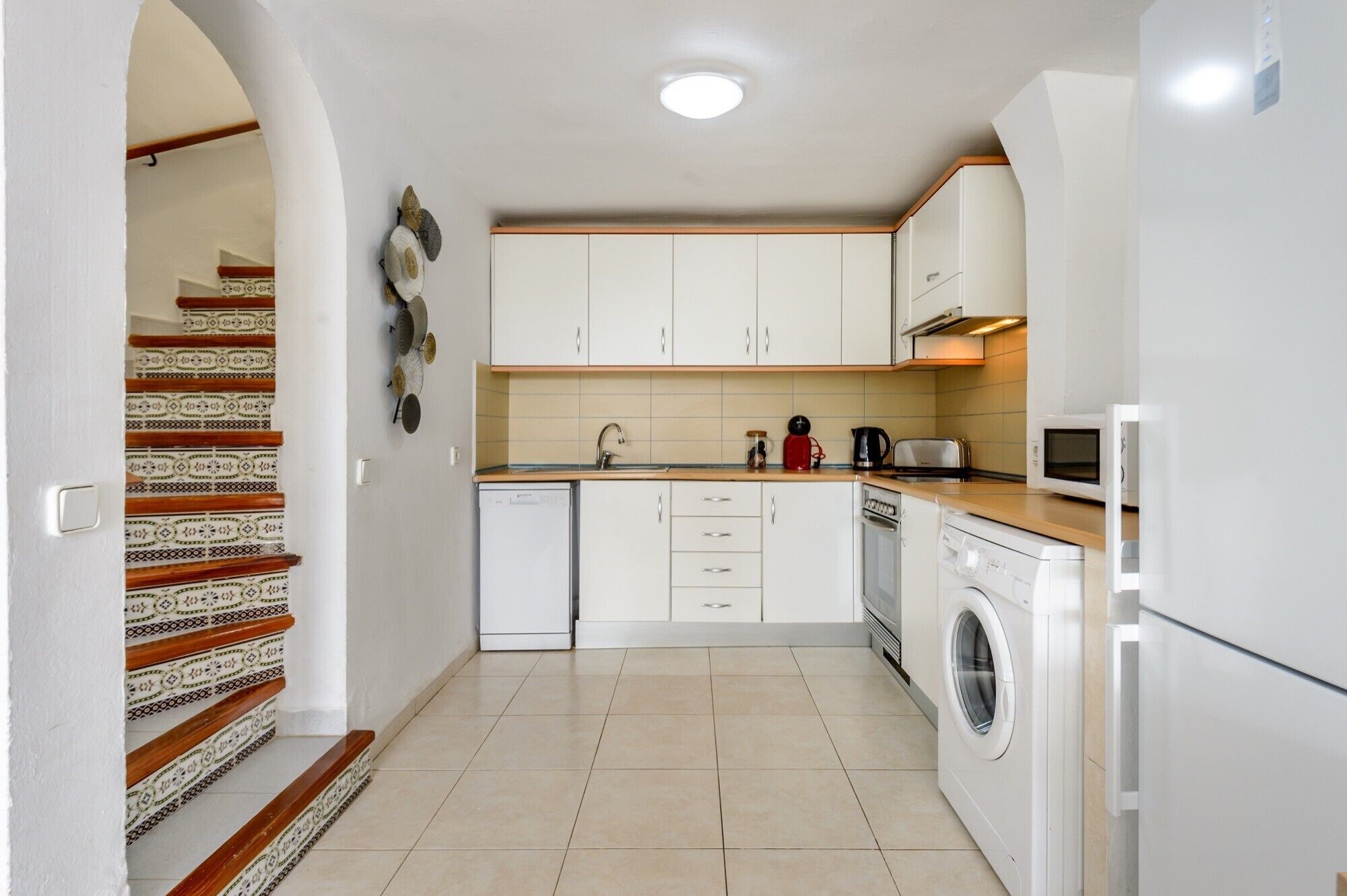 A compact kitchen with white cabinets, a washing machine, a microwave, and a toaster.