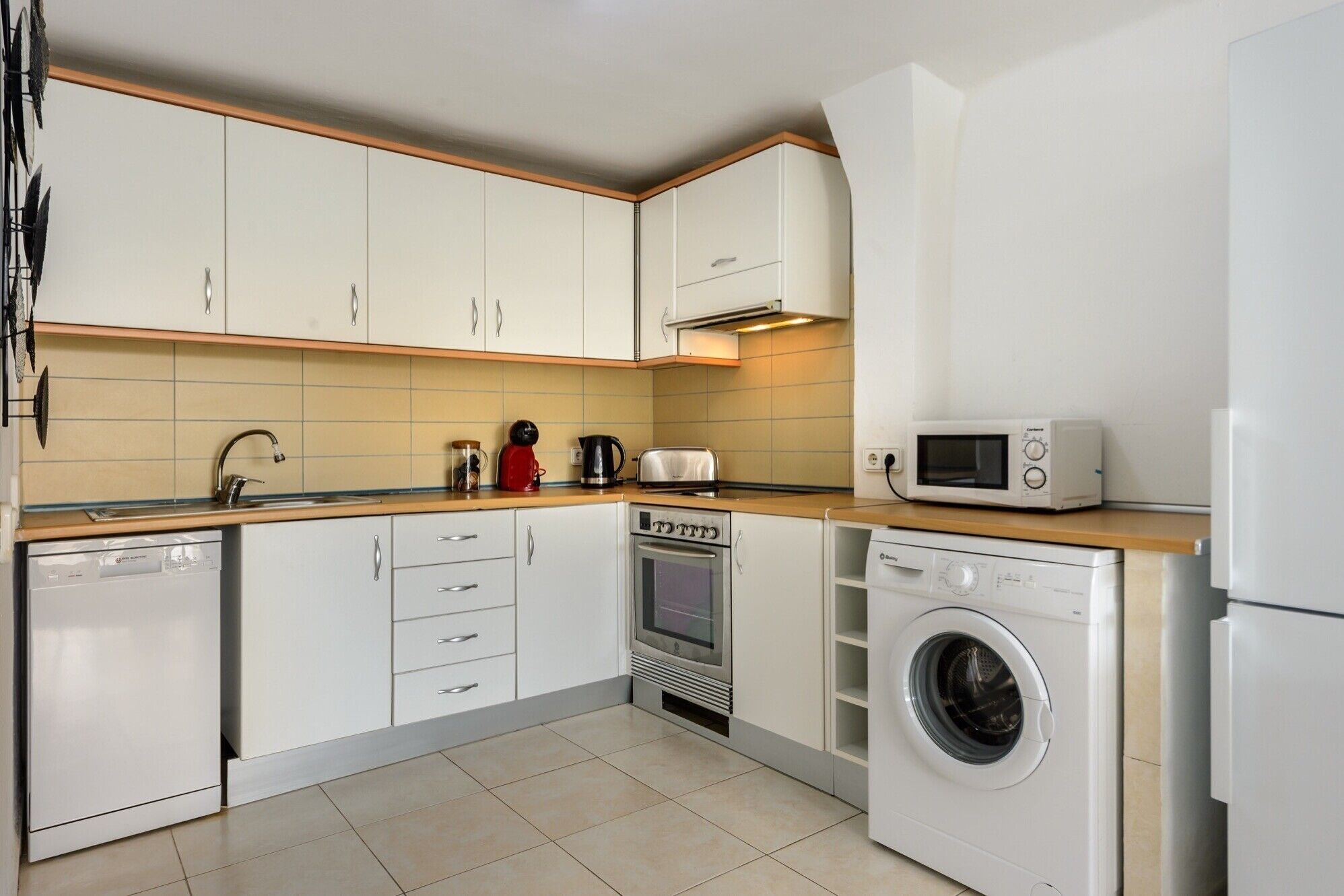 A compact kitchen with white cabinets, a microwave, a toaster, and a washing machine.