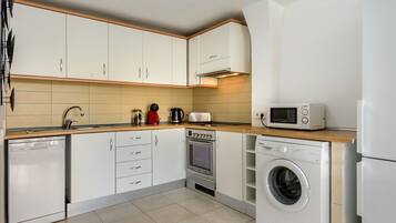 A compact kitchen with white cabinets, a microwave, a toaster, and a washing machine.