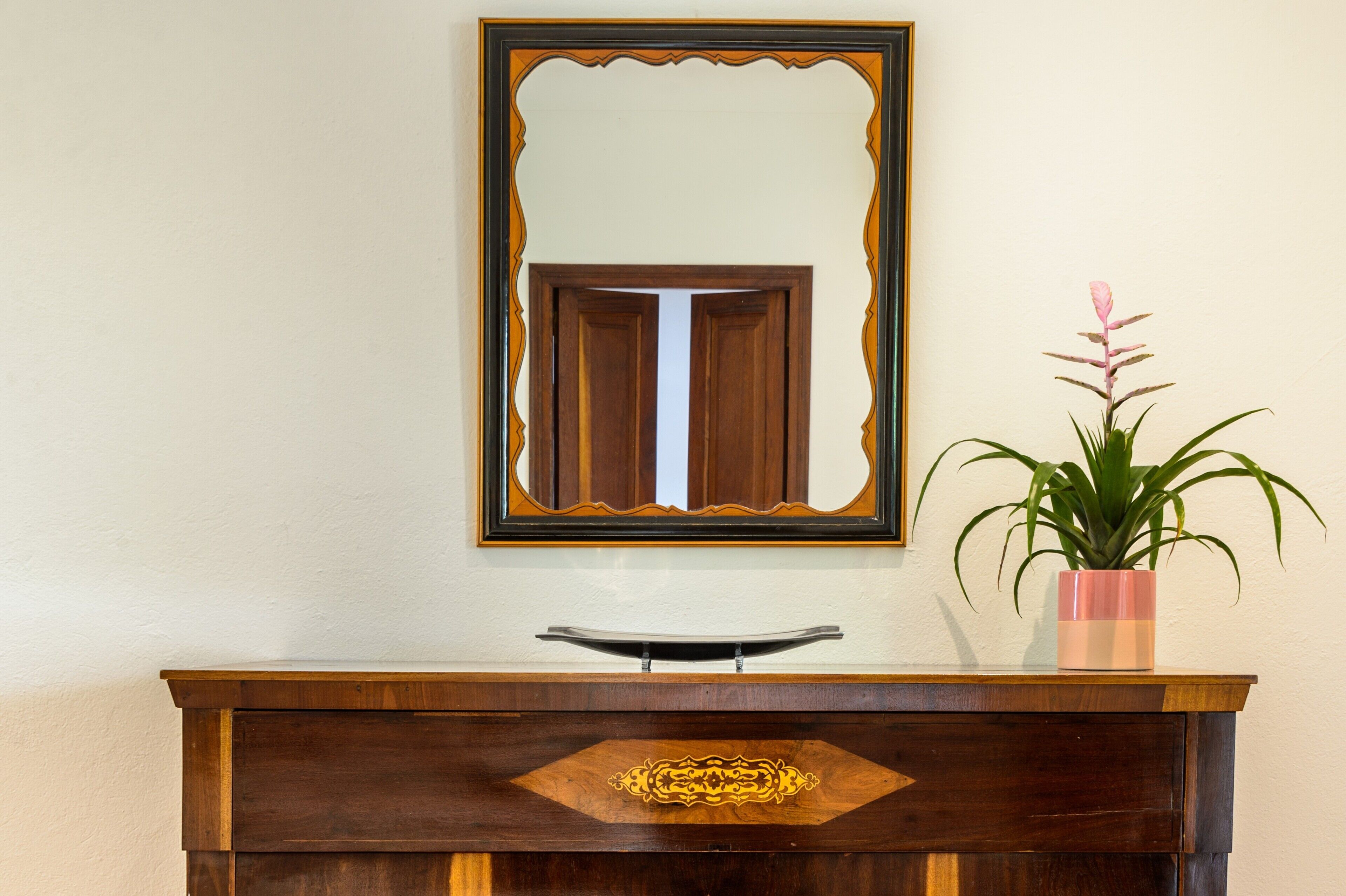 A wooden dresser with a mirror above it, a drawer with a decorative front, and a potted plant to the right.