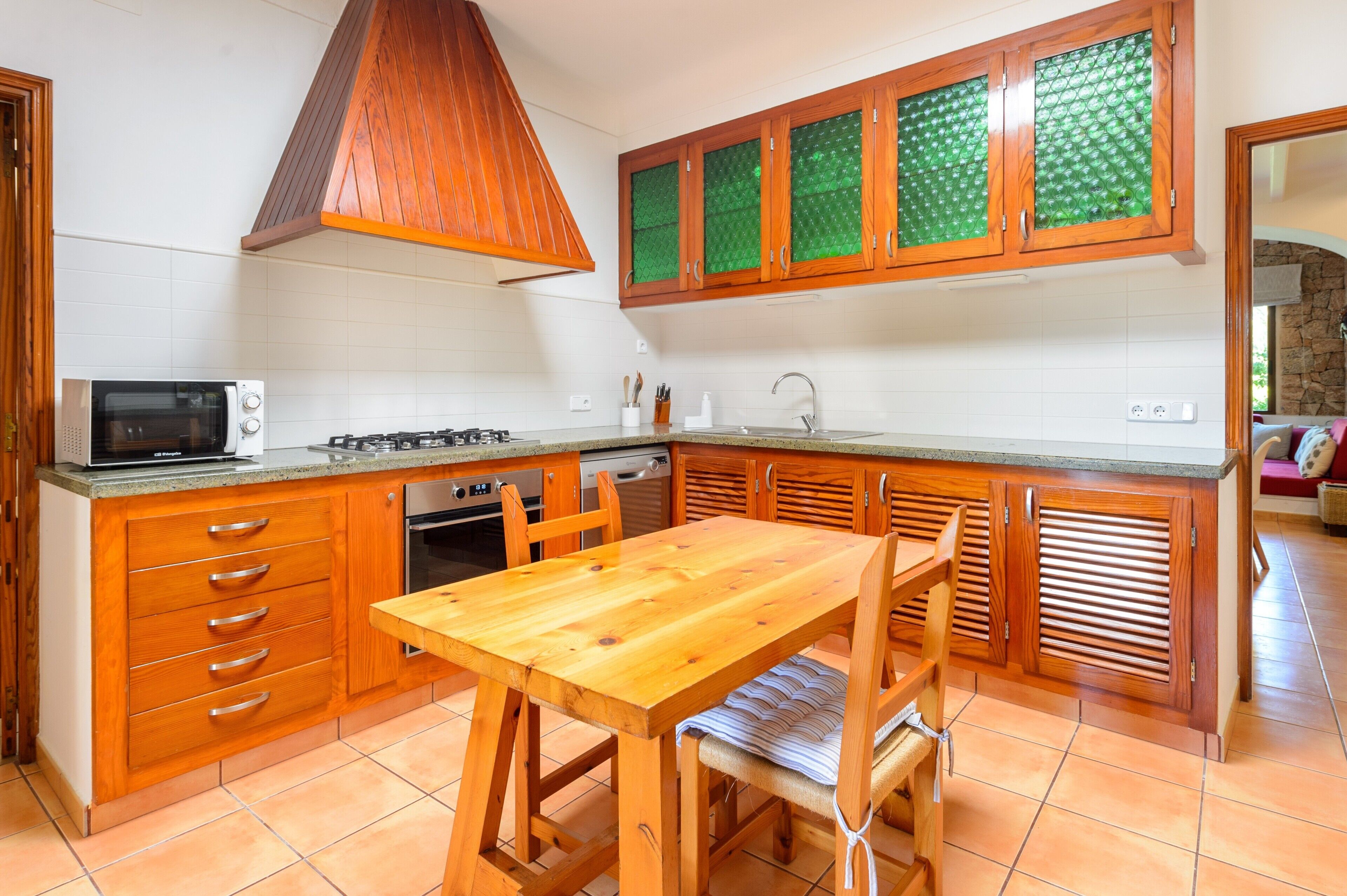 Een keuken met houten kastjes, een magnetron, een gasfornuis en een eettafel met stoelen.