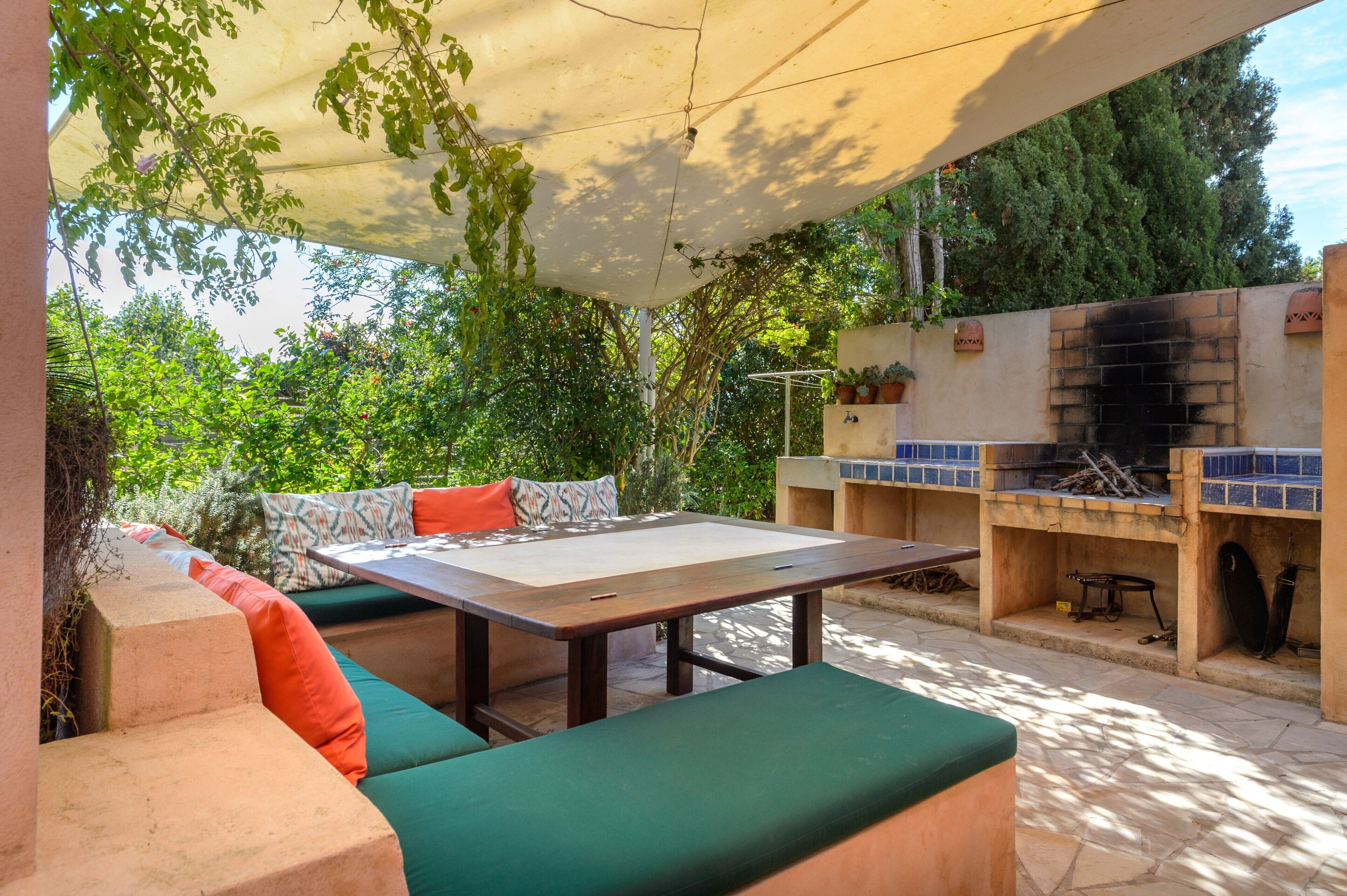 Une terrasse extérieure avec une table et des sièges confortables dotés de coussins verts, un barbecue et un mur recouvert de carreaux.
