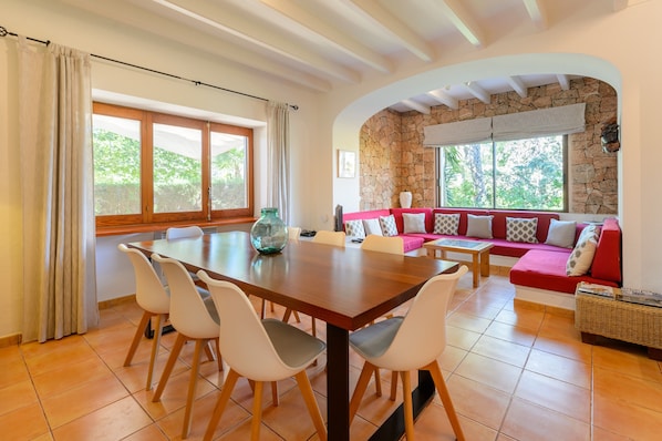 A dining area with a wooden table and chairs, a red sofa with patterned cushions, and a stone wall.