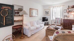 A living room with a white sofa, a television, wicker furniture, and a chalkboard with text.
