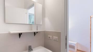 Une salle de bain avec un lavabo blanc, un miroir et une étagère au-dessus du lavabo.