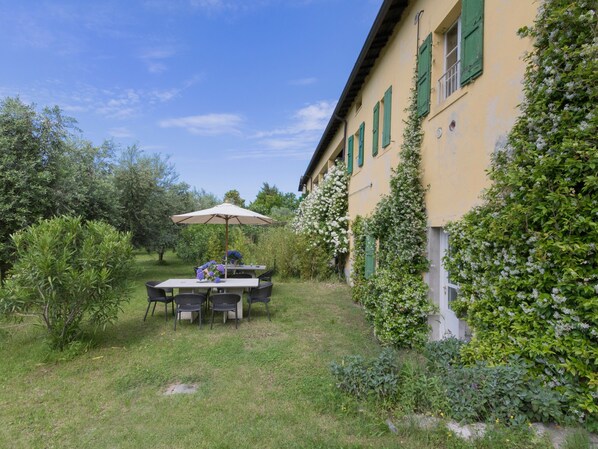 A patio with a table and chairs, surrounded by greenery and a building with green shutters.