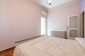 A bedroom with a bed, a dresser, a wardrobe, a window, and an air conditioning unit.