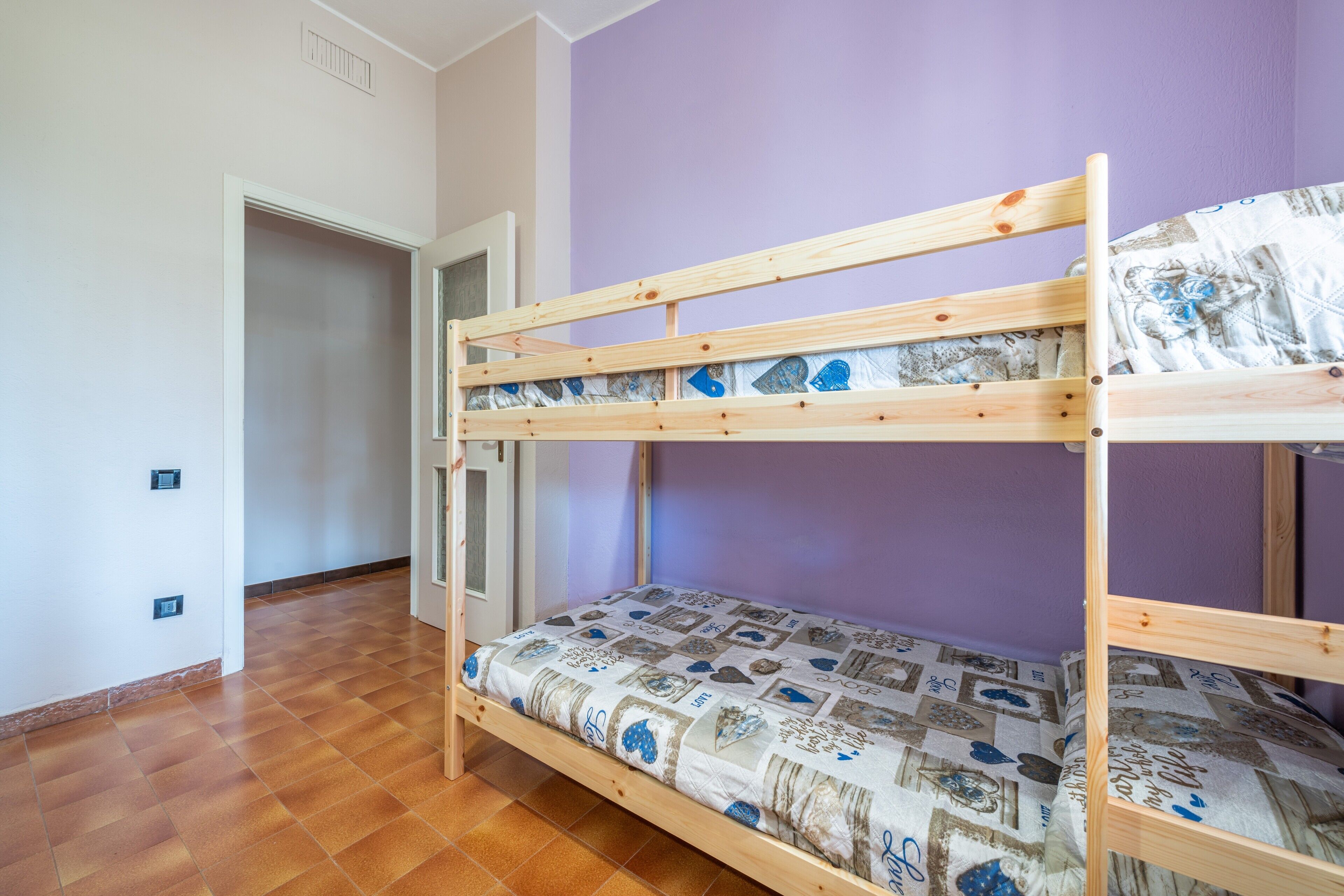 Una litera con un colchón estampado en una habitación con suelo de madera y pared morada.