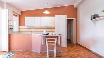 A compact kitchen with white cabinets, a small island with a chair, and a hanging light fixture.