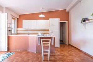 A compact kitchen with white cabinets, a small island with a chair, and a hanging light fixture.