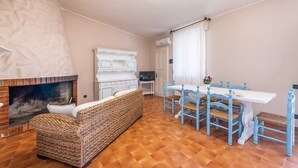 Un salon avec une cheminée, un canapé, une table à manger avec des chaises et un téléviseur.