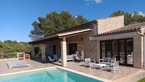 Zona junto a la piscina con un edificio de piedra, mobiliario exterior y una vista despejada del paisaje circundante.