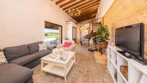 Una sala de estar con sofá, mesa de centro, televisor, escalera y plantas en macetas.
