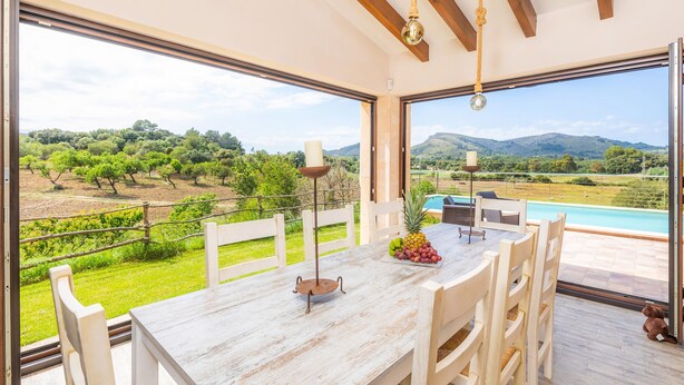 Un comedor con mesa, sillas, una vela y vistas a una piscina y al paisaje.