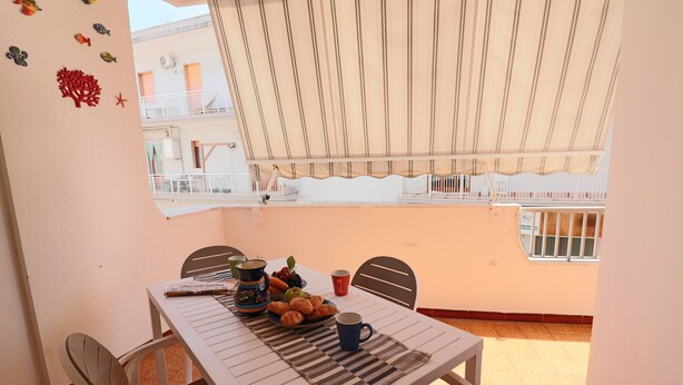 Een eettafel met stoelen, een geribbelde placemat, een bord met croissants, een kopje en een schaal fruit.