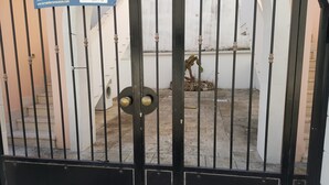 Une entrée fermée par un portail en métal, un lave-linge et un escalier menant à l’étage supérieur.