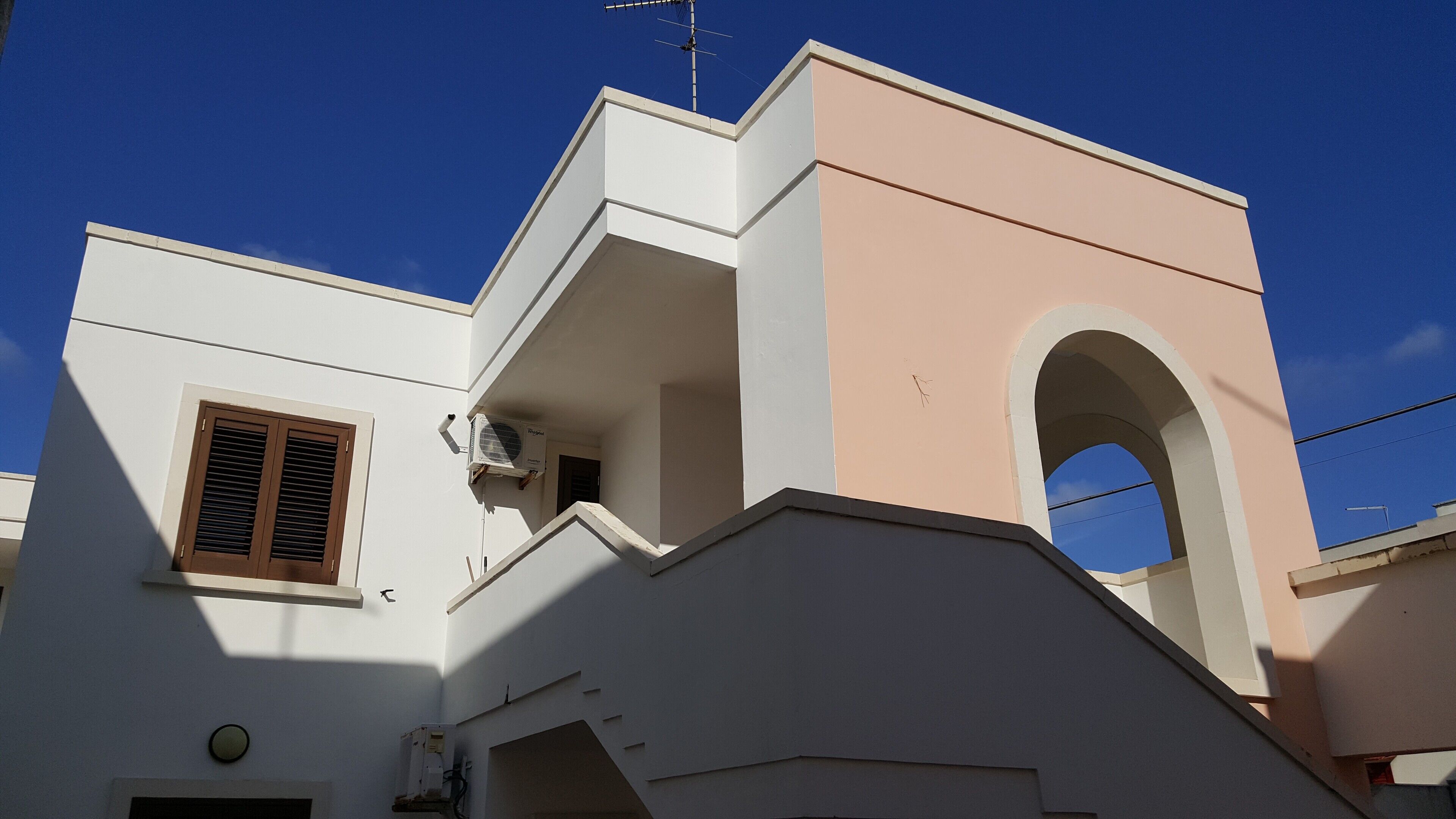 Ein Gebäude mit weißer und pfirsichfarbener Fassade, einer sichtbaren Antenne und einem Fenster mit Rollläden.