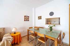 A dining area with a table, chairs, a lamp, and a small side table with a basket.