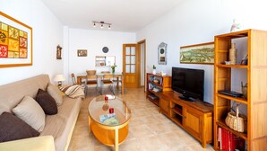 Ein Wohnzimmer mit einer Couch, Couchtisch, Fernseher, Holzregal und einem Essbereich mit Stühlen und Tisch.