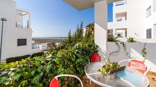 Ein Balkon mit Glastisch und Stühlen, Blick aufs Meer und weiße Gebäude mit Balkonen.