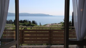 A balcony with a wooden bench, overlooking a body of water and distant hills.