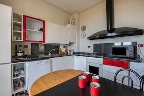 A modern kitchen with white cabinets, a black countertop, and a red accent wall.